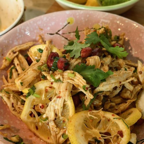 Lemon shredded chicken breast with lemon slices, peanuts, cilantro, and sesame seeds on a white plate