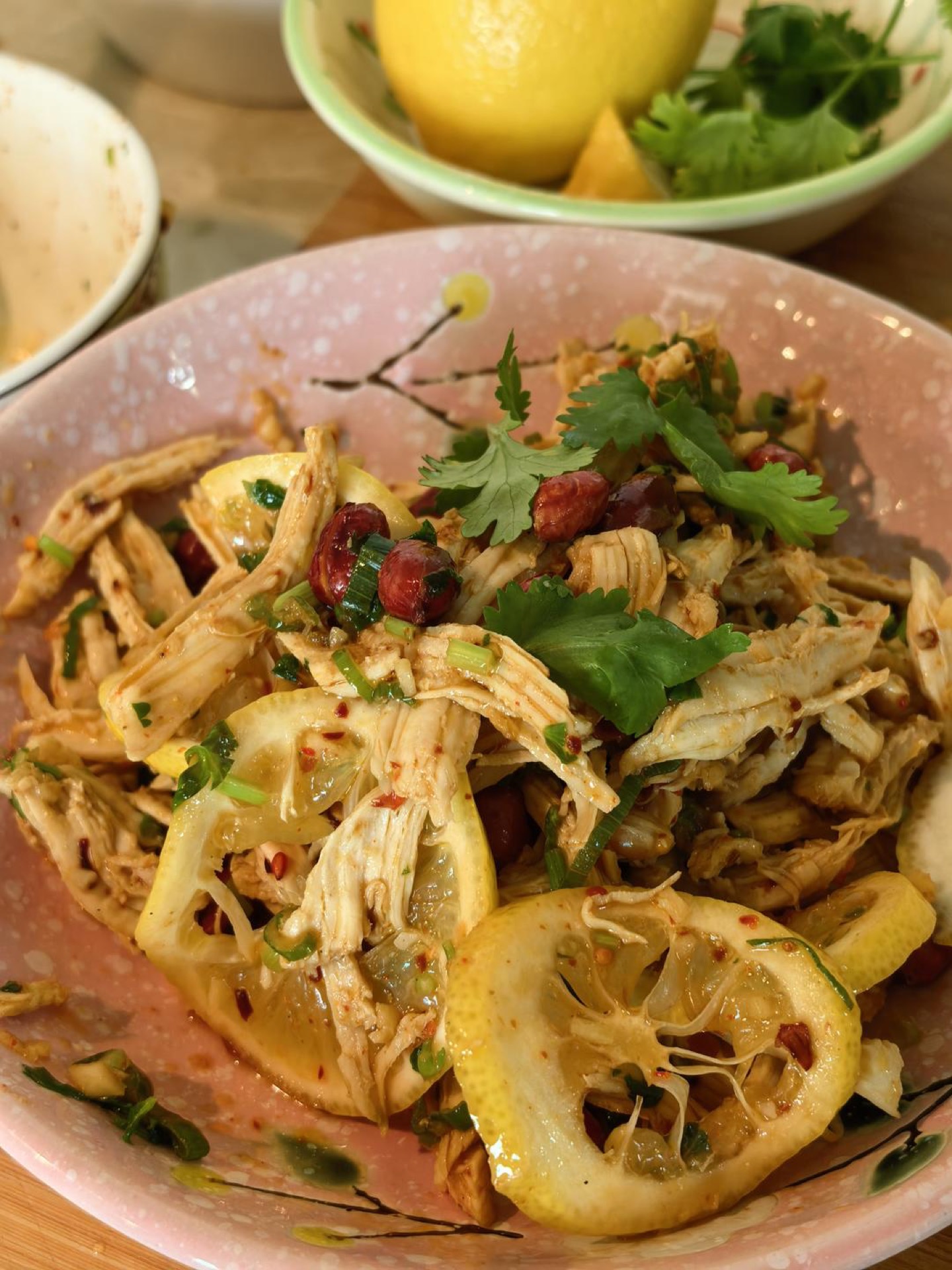 Lemon shredded chicken breast with lemon slices, peanuts, cilantro, and sesame seeds on a white plate