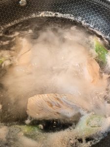 Chicken breasts poaching in a pot with scallion and ginger