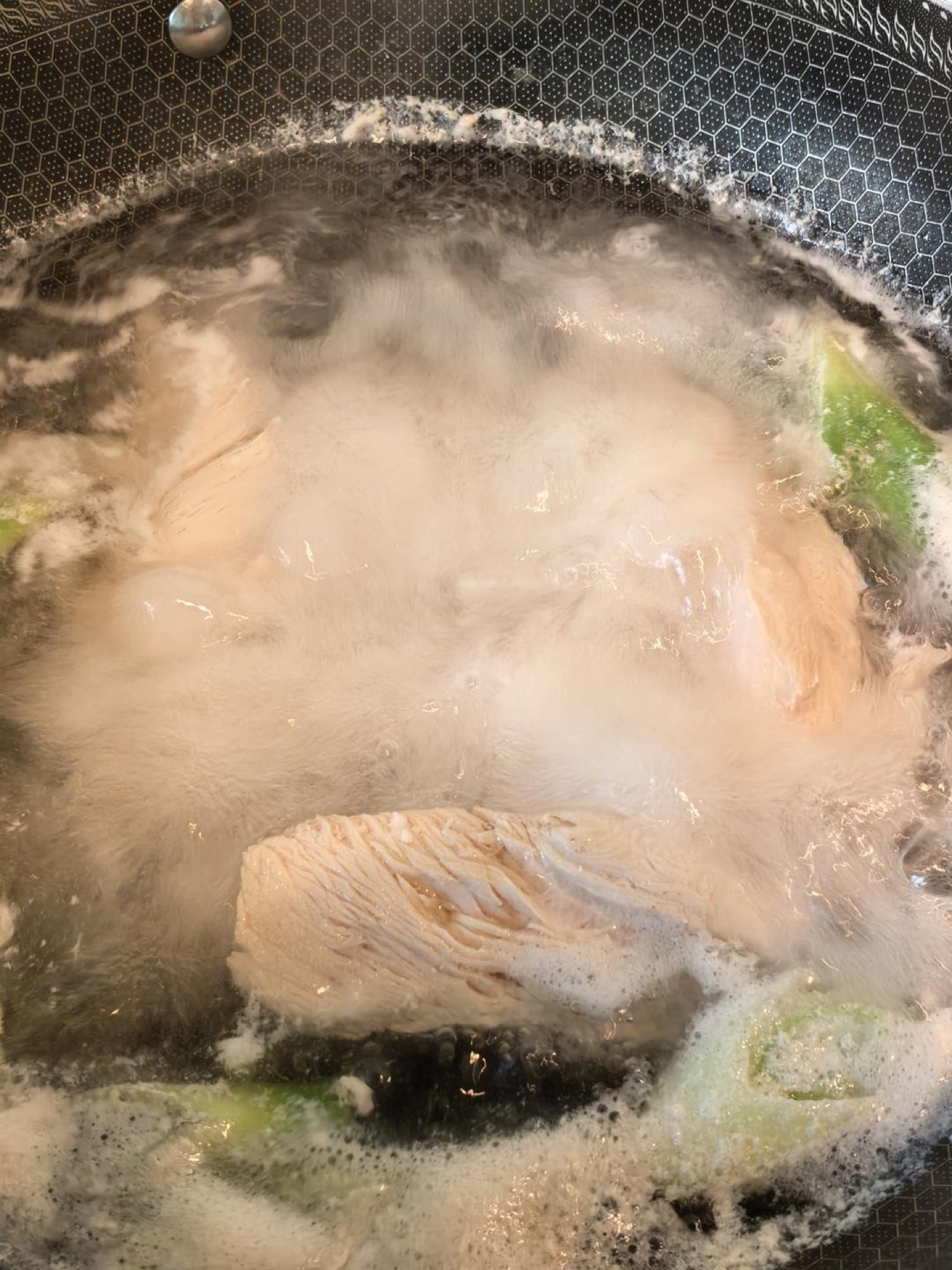 Chicken breasts poaching in a pot with scallion and ginger