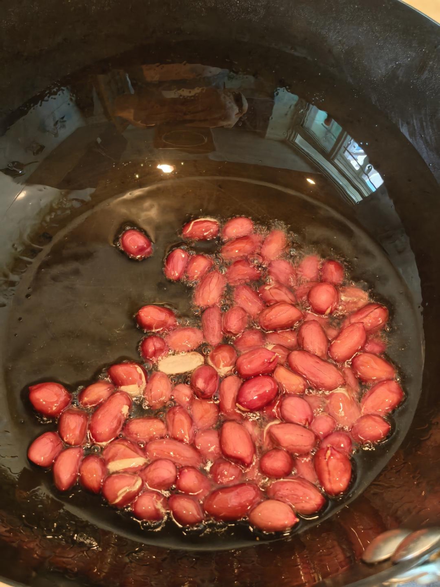 Golden fried peanuts draining on a slotted spoon