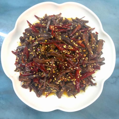 Cold-fried beef strips (leng chi niu rou) piled in a bowl with dried chilies and sesame seeds
