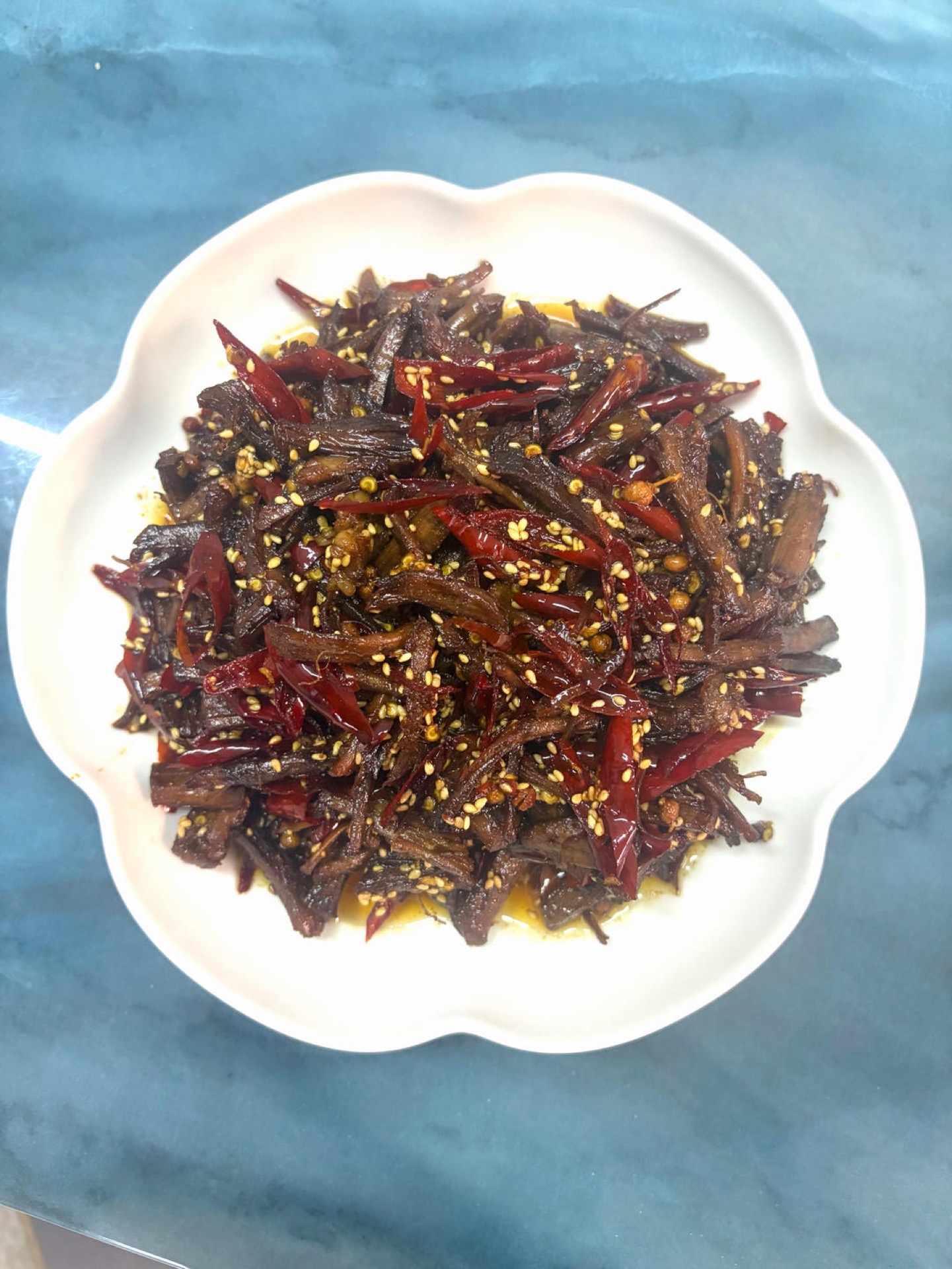 Cold-fried beef strips (leng chi niu rou) piled in a bowl with dried chilies and sesame seeds