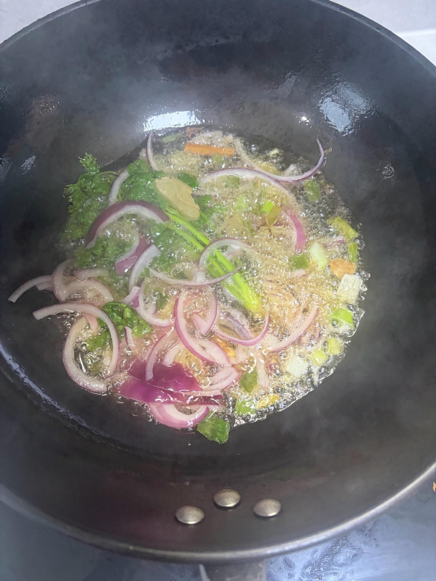 Pour oil into the wok, a little more than you would for a normal stir-fry but not too much, otherwise the finished dish will be swimming in oil. Add the cilantro, onion, bay leaves