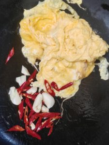 Heat a little oil in the wok and fry the eggs until set, then add the small red chili and the garlic.