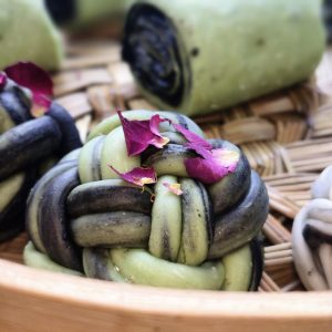 Matcha rose steamed buns stacked in a bamboo steamer, topped with dried rose petals and osmanthus