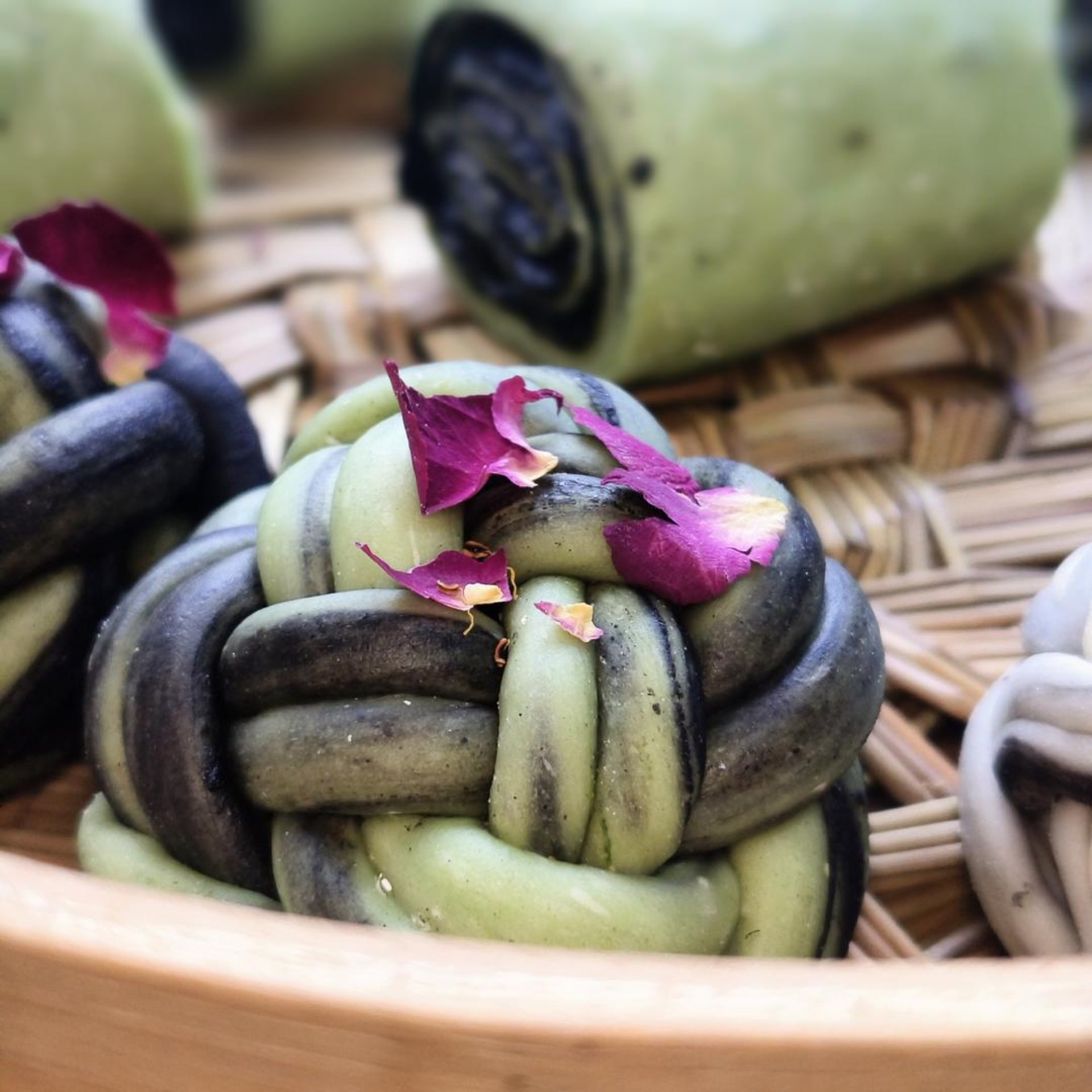 Matcha rose steamed buns stacked in a bamboo steamer, topped with dried rose petals and osmanthus