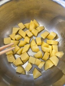 Peel the potatoes, cut them into 1-inch chunks, add them to the pot, and toss so every piece is slicked with oil, then spread them into a flat, even layer across the bottom.