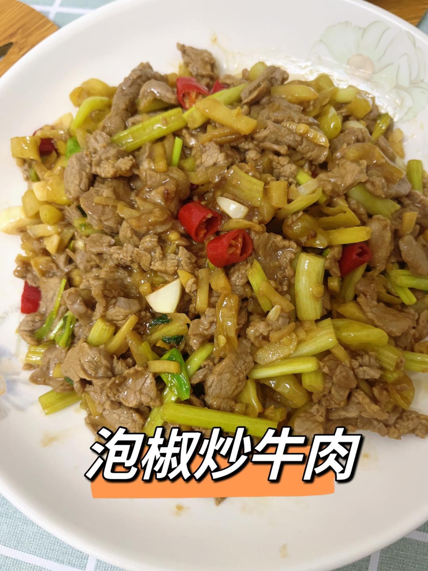 Pickled pepper stir-fried beef with tender beef slices, pickled chilies, and celery served on a white plate