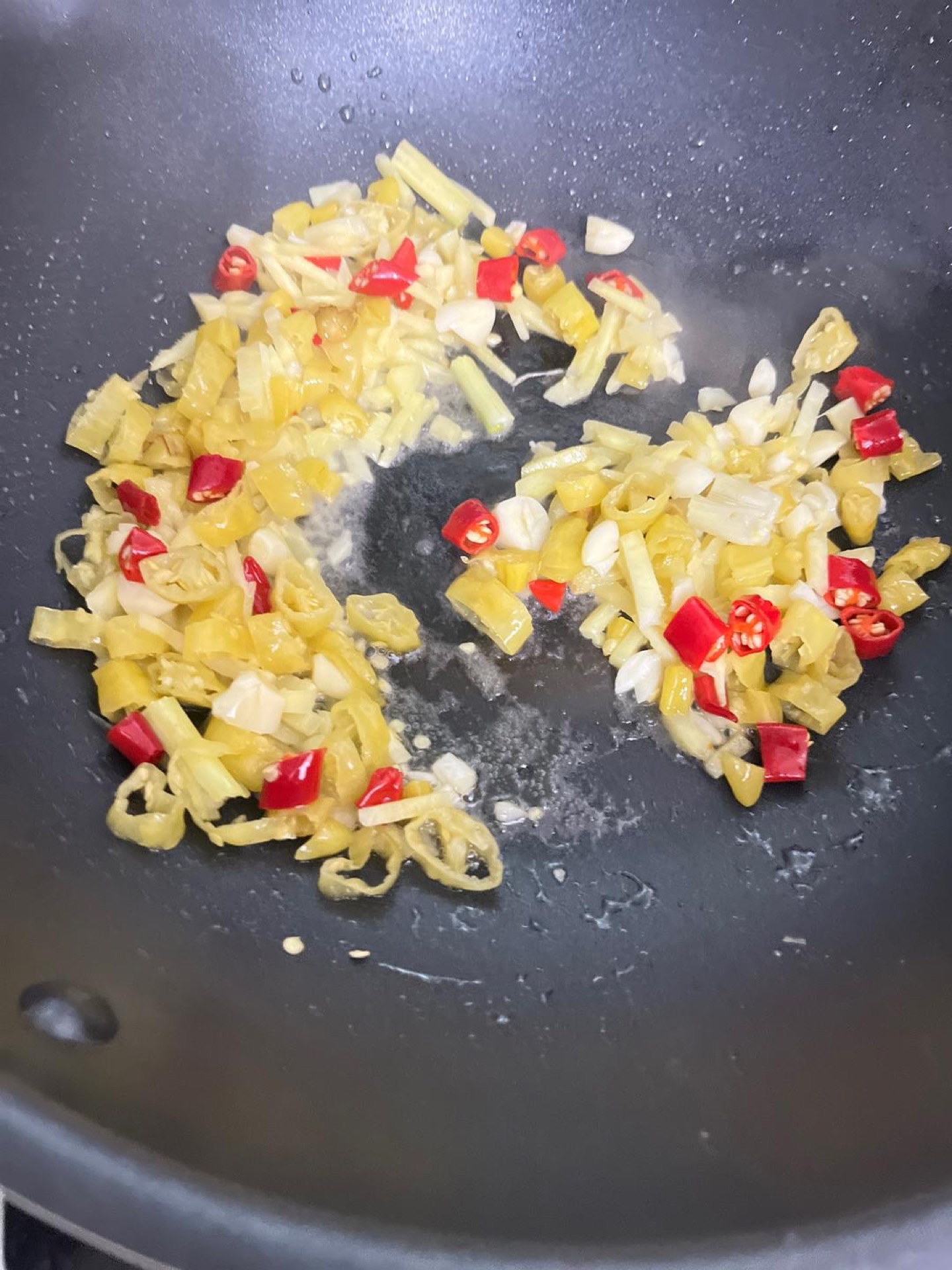 Heat oil in the wok until shimmering, then add the ginger, garlic, pickled chilies, and bird's eye chilies in order, stir-frying until the aroma is sharp and pungent.