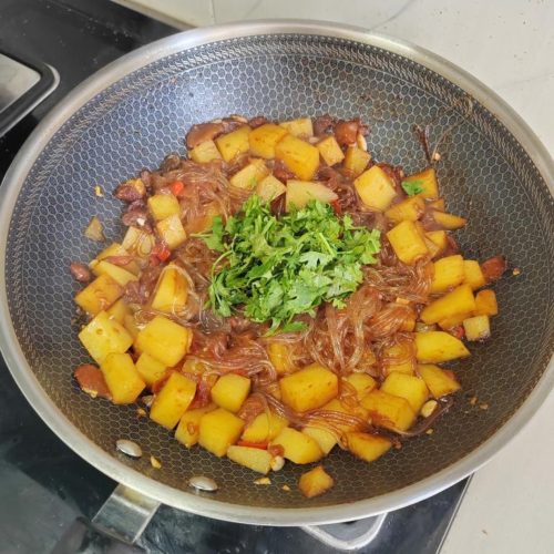 Potato tomato stewed vermicelli in a dark pan, glossy with tomato sauce