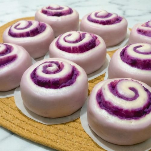 Purple sweet potato steamed rolls on a bamboo steamer, torn open to show the swirled crumb