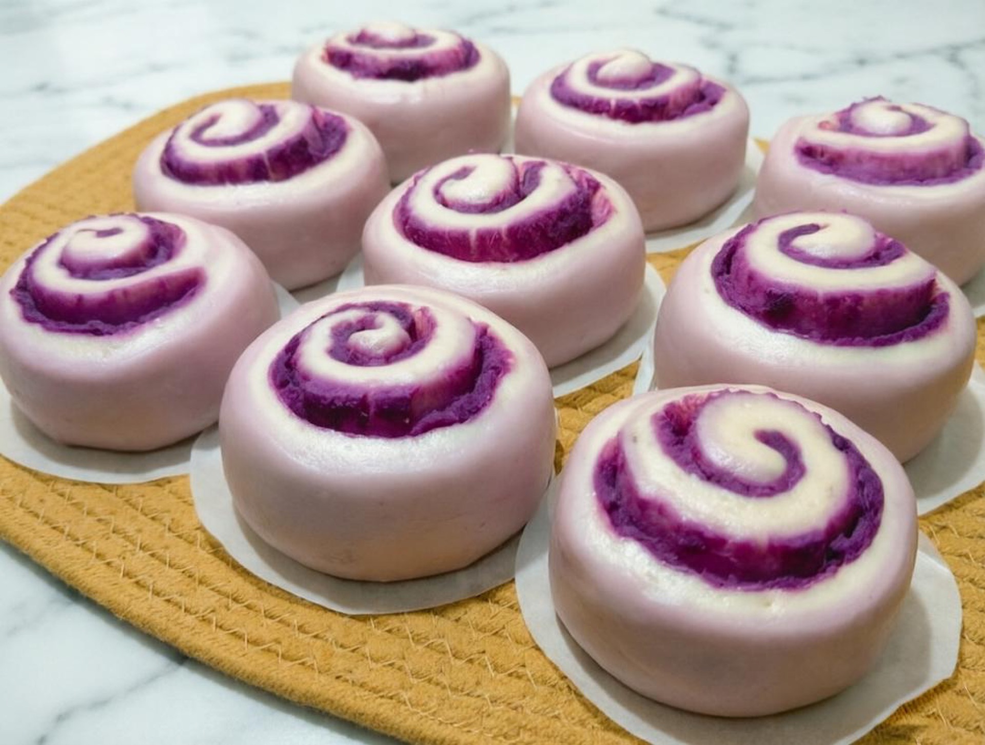 Purple sweet potato steamed rolls on a bamboo steamer, torn open to show the swirled crumb