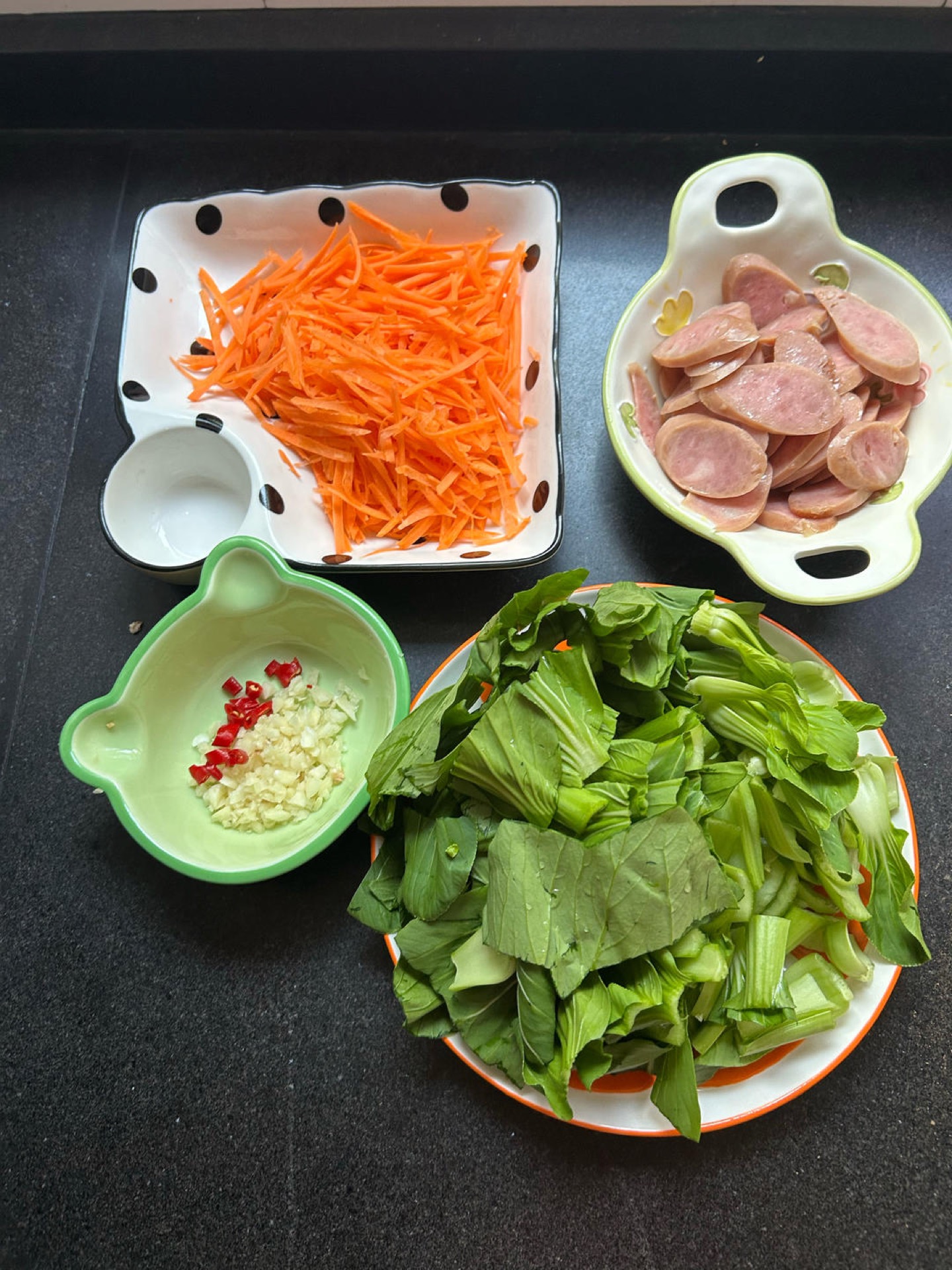 Chopped carrot, bok choy, garlic, and chili prepped on a cutting board