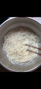 Drained rice noodles tossed with oil in a bowl to prevent sticking