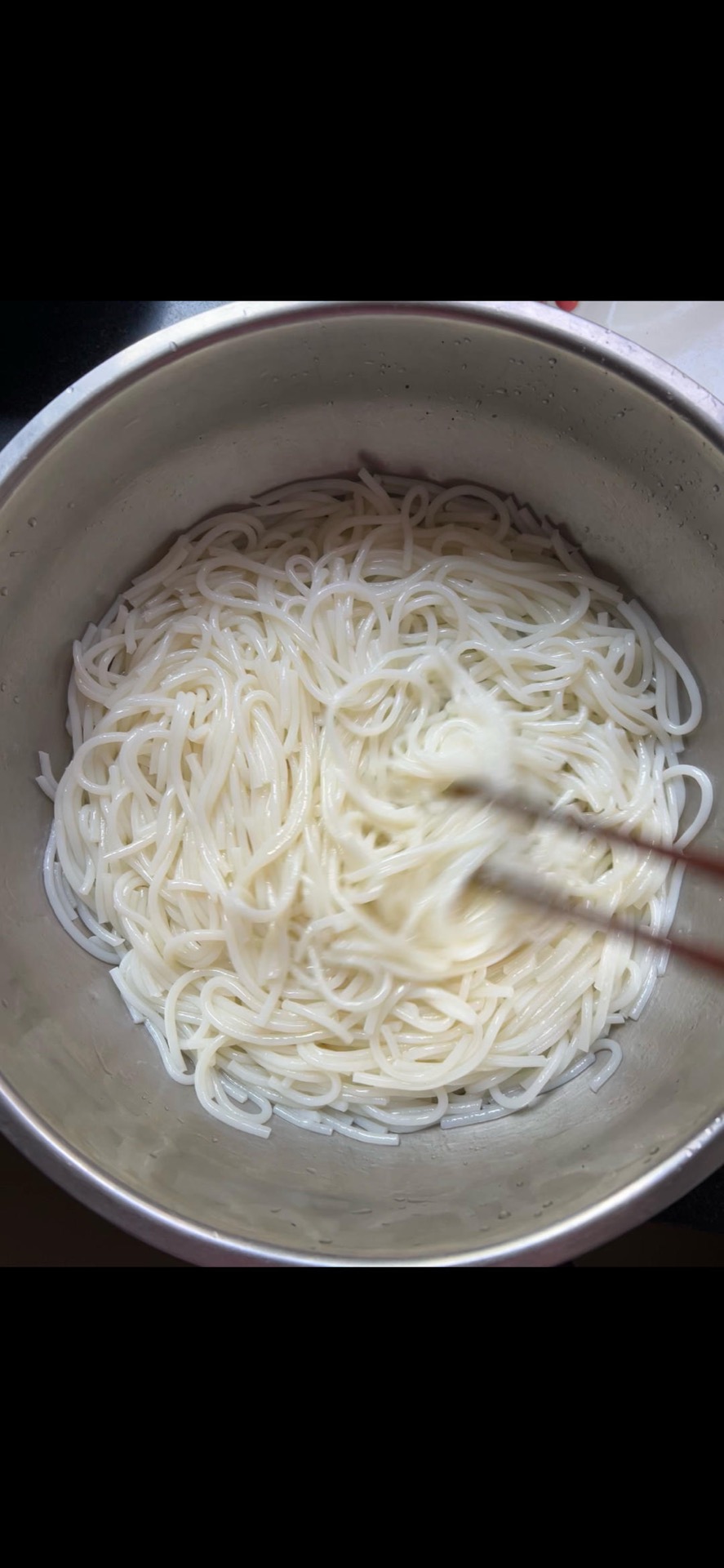 Drained rice noodles tossed with oil in a bowl to prevent sticking