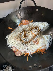 Rice noodles being tossed with soy sauce in a wok using chopsticks