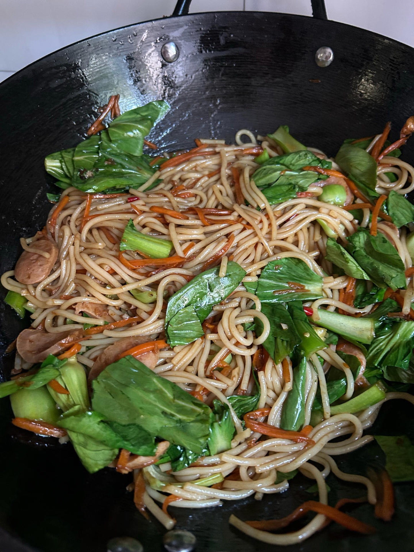 Bok choy being folded into stir-fried rice noodles in a wok