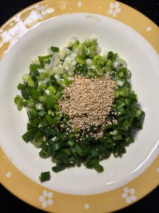 Rinse a bunch of scallions clean and chop them into small pieces, add 2 tbsp white sesame seeds, and if you like heat add chopped bird's eye chilies — I left them out because kids