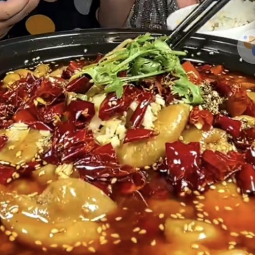 Poached pork intestines in a clay pot topped with dried chilies, Sichuan peppercorns, sesame seeds, and cilantro