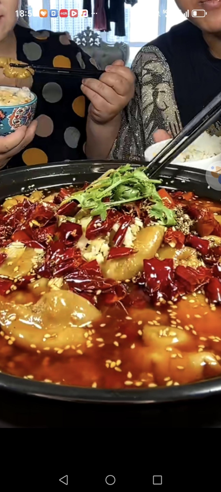 Poached pork intestines in a clay pot topped with dried chilies, Sichuan peppercorns, sesame seeds, and cilantro