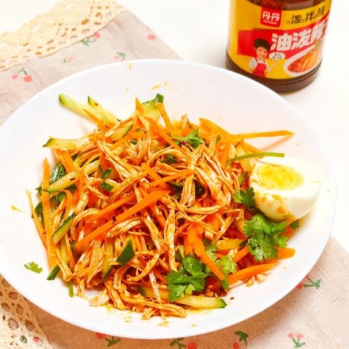 Spicy cold shredded chicken with cucumber, carrot, and chili oil dressing in a white bowl