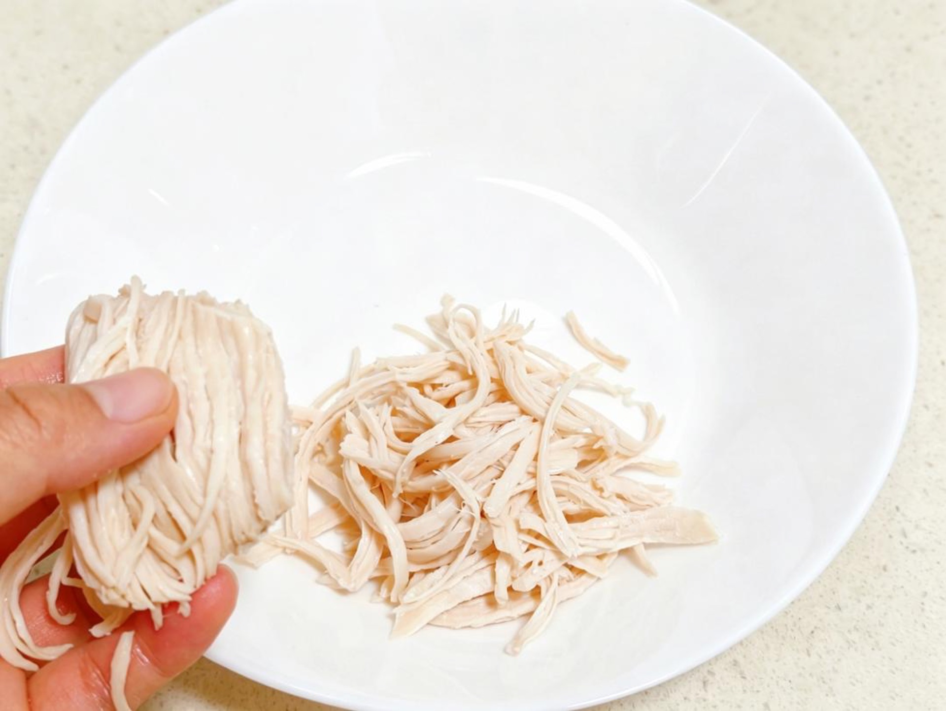 Lift the cooled breast from the ice water, pat it dry, and tear it apart along the grain into fine, even shreds with your fingers.