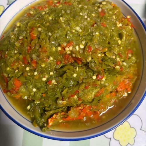 Steamed eggplant with green chili sauce in a bowl, topped with cilantro and chopped green chilies