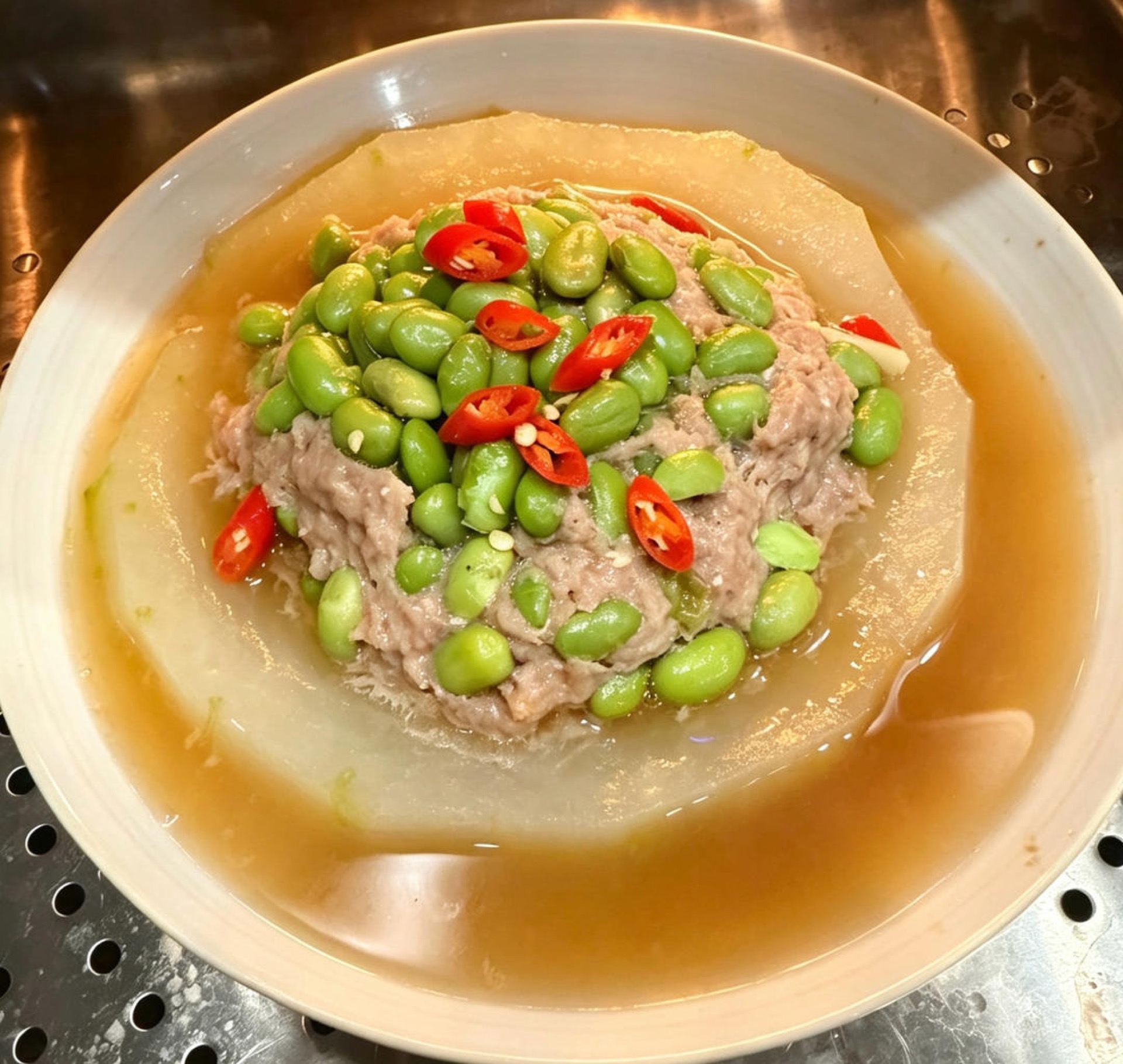 Steamed winter melon with pork and salted egg yolk topped with edamame and scallions on a white plate