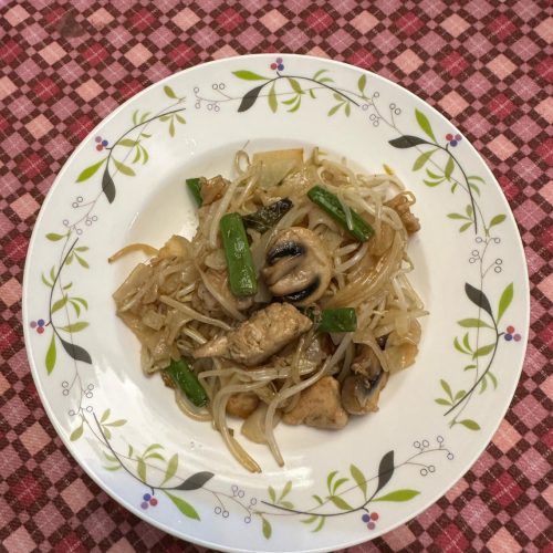 Stir-fried chicken with rice noodles in a wok with beansprouts and scallions