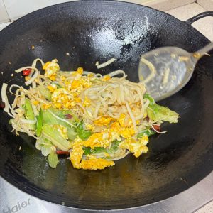 Returning the egg to the wok with the noodles