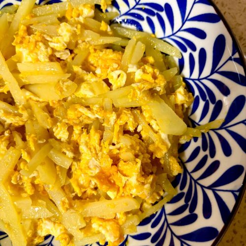 Stir-fried potato and egg served on a white plate with soft julienned potato and fluffy scrambled egg