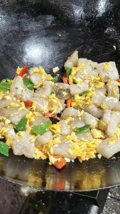 Tip the starch pieces into a slotted spoon and shake off the excess starch, push the scrambled egg to one side of the wok, add the minced garlic, then the green and red pepper piec
