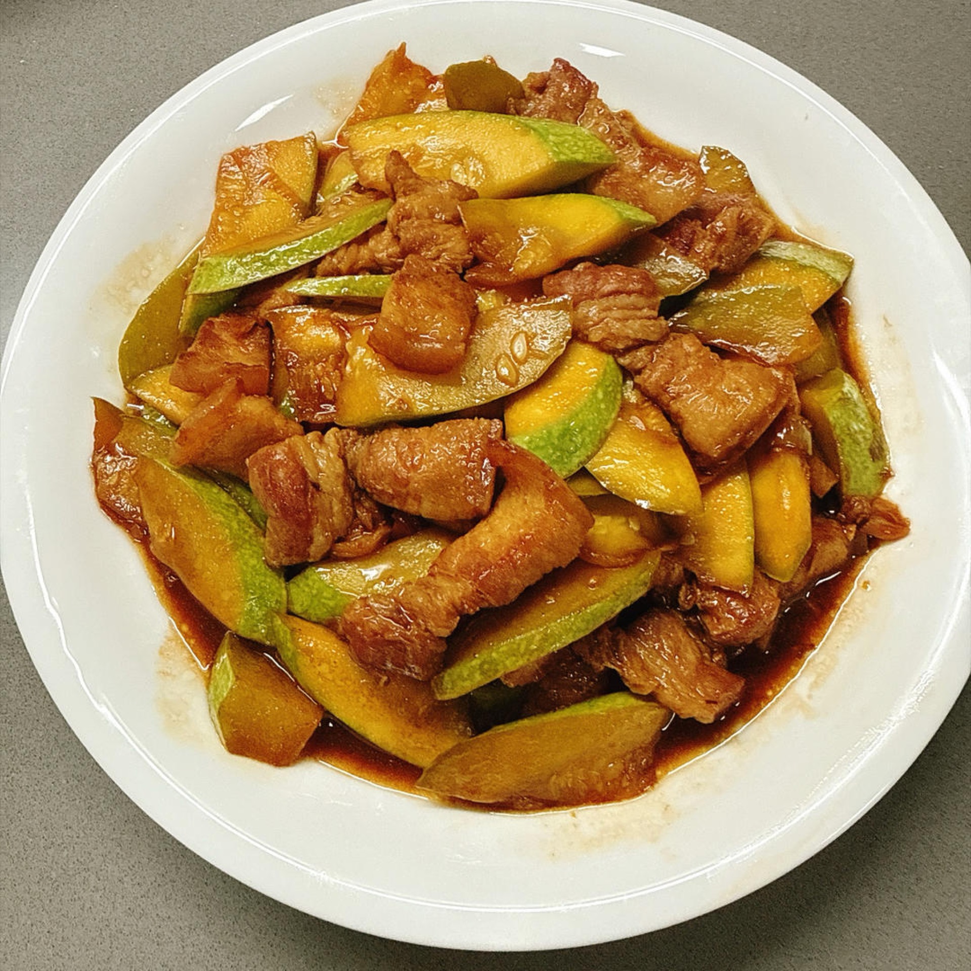 Stir-fried zucchini with pork belly in a wok, glossy with sauce and scattered with scallions