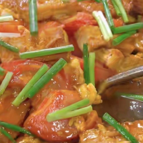 Tomato braised tofu with eggs in a wok, golden tofu cubes and tomato wedges coated in glossy red sauce
