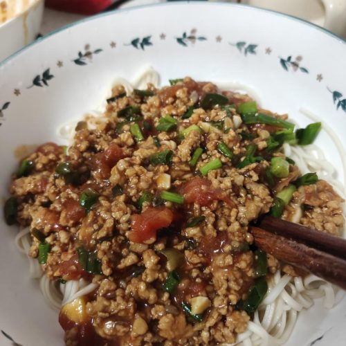 A bowl of tomato meat sauce noodles topped with glossy pork and tomato sauce and sliced scallions