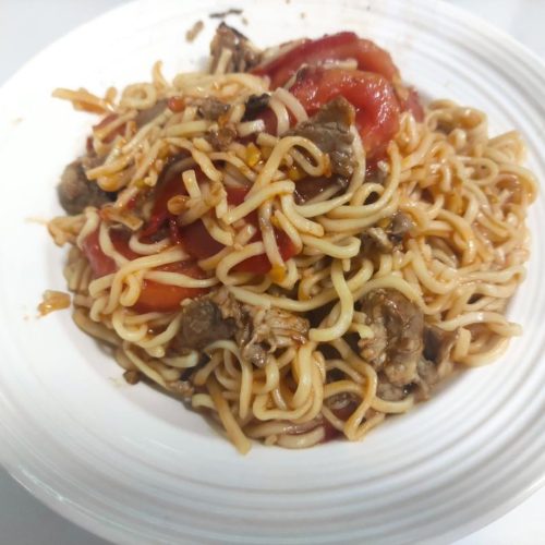 A plate of tomato pork stir-fried noodles with glossy tomato sauce and tender pork slices