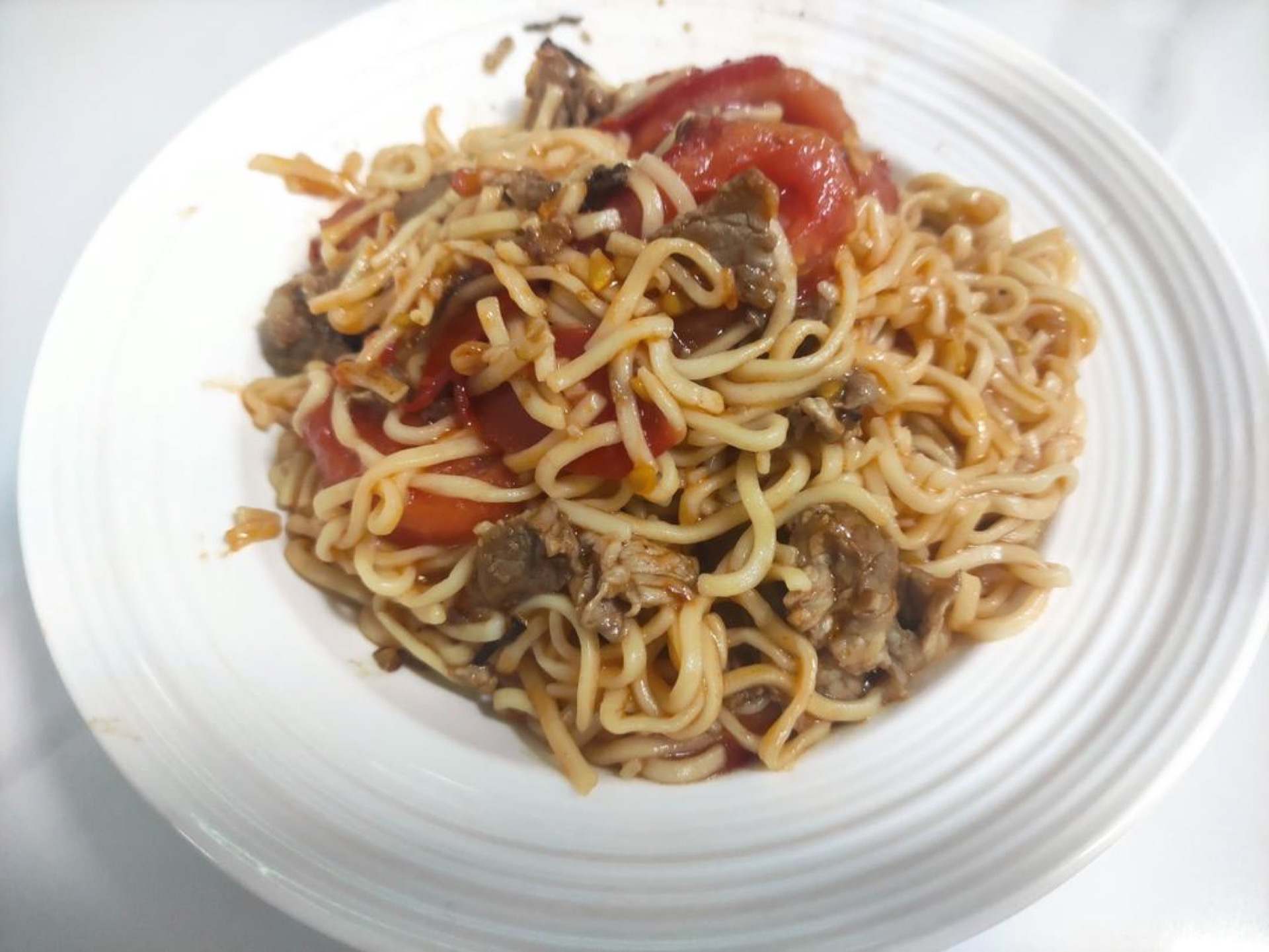 A plate of tomato pork stir-fried noodles with glossy tomato sauce and tender pork slices