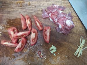 Cut the tomato into wedges, slice the pork, cut the chili into rings, mince the garlic, and julienne the ginger.