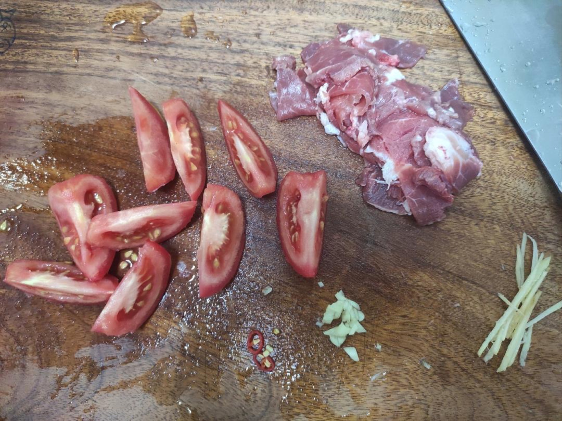 Cut the tomato into wedges, slice the pork, cut the chili into rings, mince the garlic, and julienne the ginger.