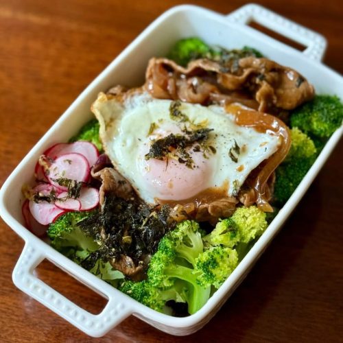 Wagyu beef over multigrain rice in a large bowl with broccoli, pickled radish, and a fried egg