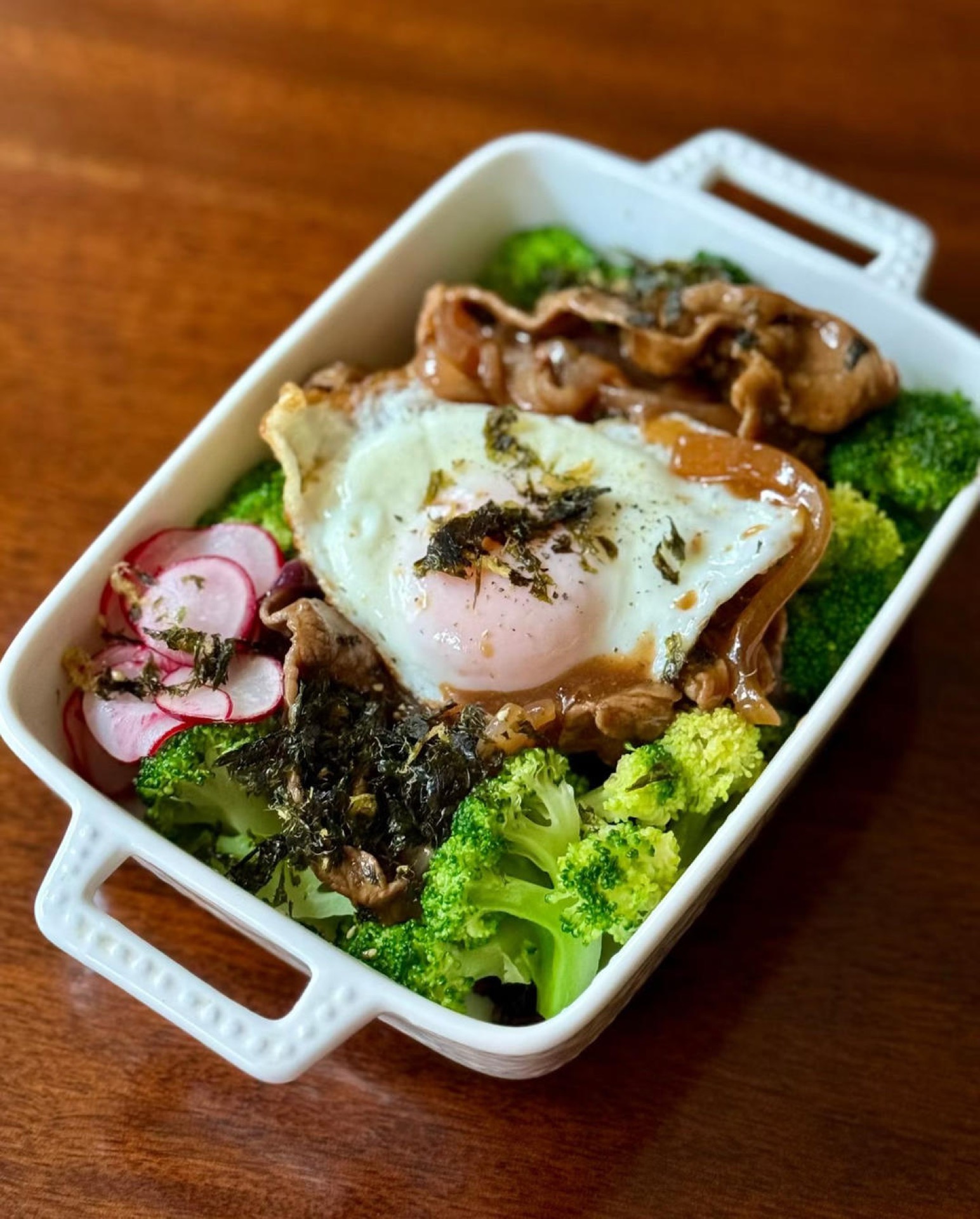 Wagyu beef over multigrain rice in a large bowl with broccoli, pickled radish, and a fried egg