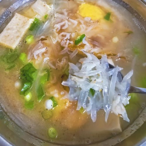 A bowl of white radish egg soup with shredded daikon, golden egg pieces and scallions in a light broth