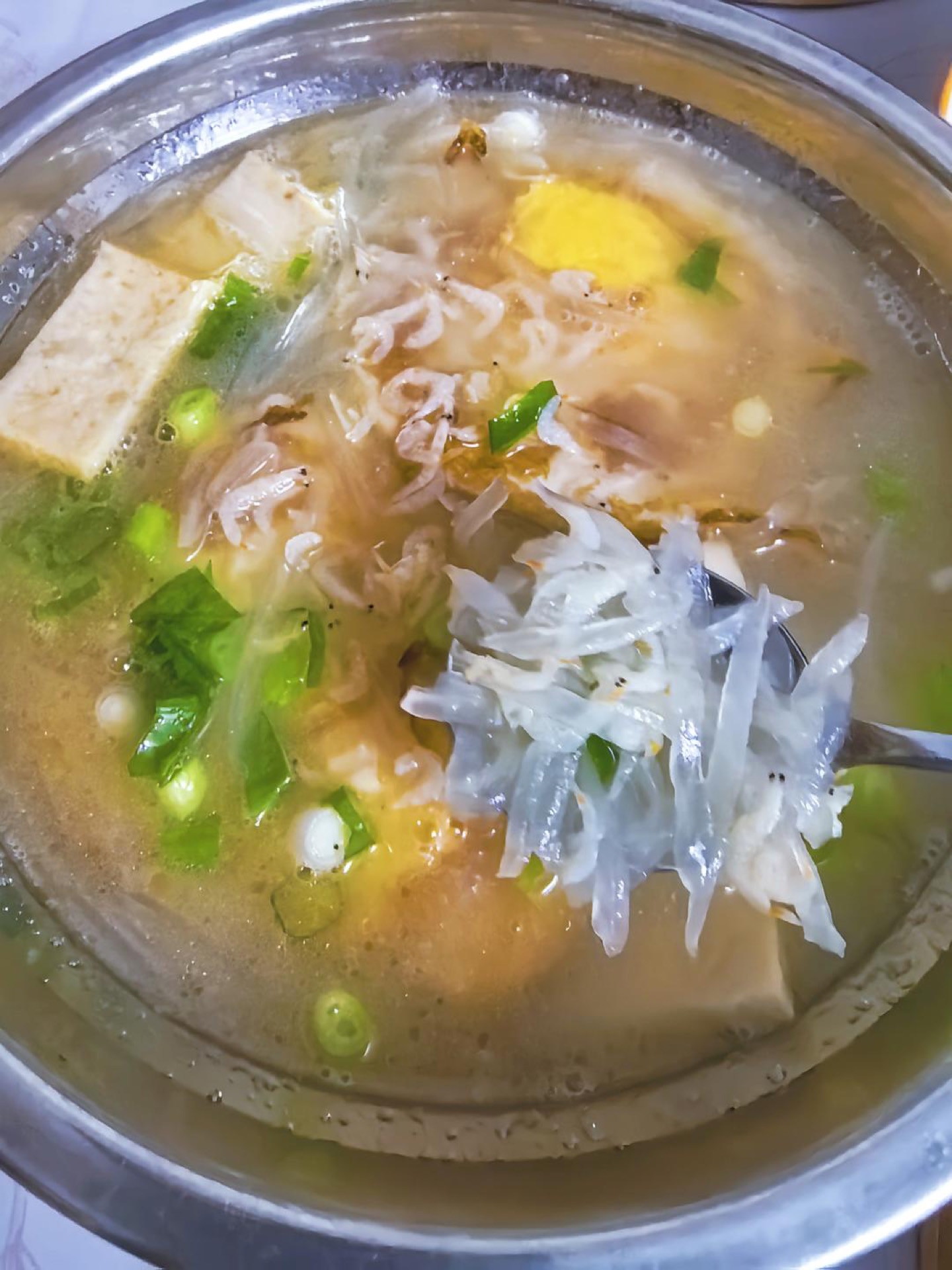 A bowl of white radish egg soup with shredded daikon, golden egg pieces and scallions in a light broth