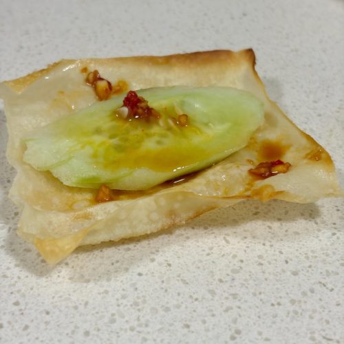 Wonton skin cucumber bites on a plate, brushed with chili garlic sauce and topped with cucumber slices