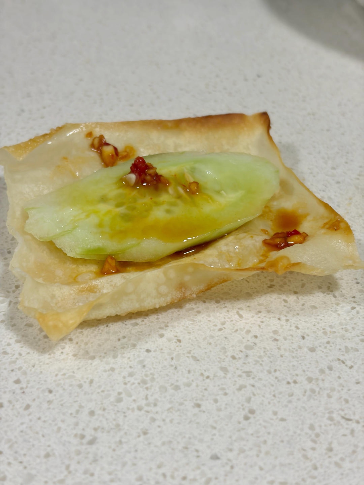 Wonton skin cucumber bites on a plate, brushed with chili garlic sauce and topped with cucumber slices