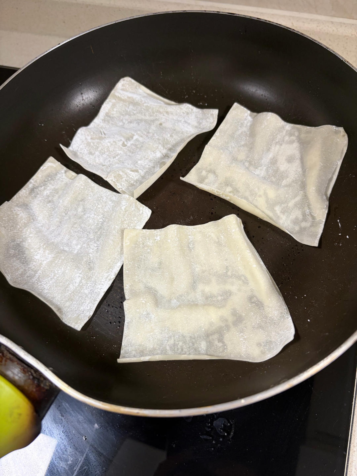 Wonton wrappers frying in a lightly oiled pan until golden