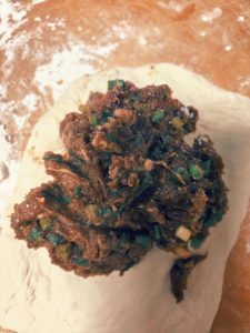 Place 70 g of filling in the center, then use your hands to gather the dough up slowly, sealing it like a baozi. Press it flat on the board into a pie shape, pressing gently by han