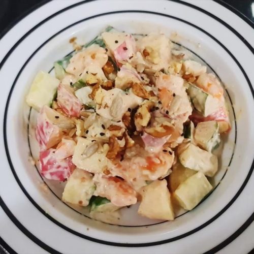 Yogurt apple cucumber shrimp salad in a wide white bowl topped with chopped nuts