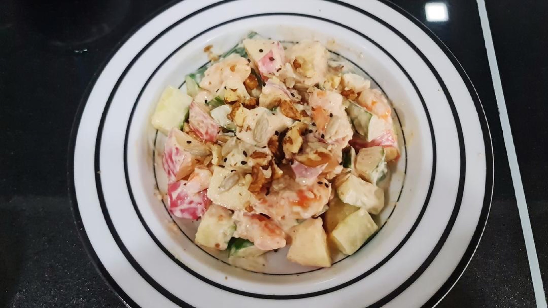 Yogurt apple cucumber shrimp salad in a wide white bowl topped with chopped nuts
